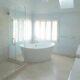 Renovated bathroom with white soaking tub, large glass door shower, white countertops and large windows