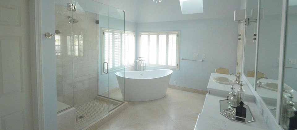 Renovated bathroom with white soaking tub, large glass door shower, white countertops and large windows
