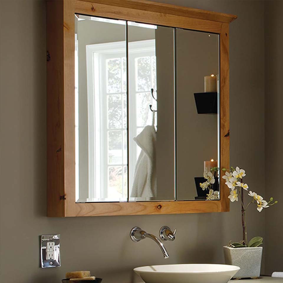 Over the sink bathroom cabinet in light wood with three mirrors.