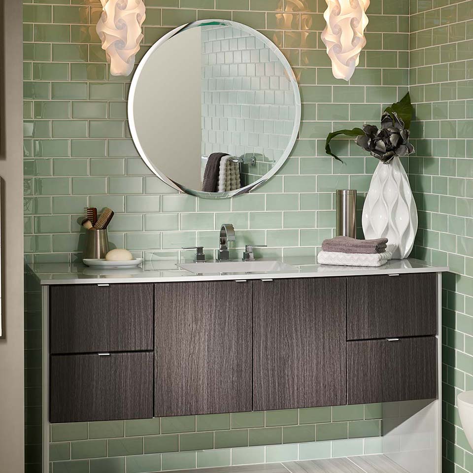 Dark vanity with modern design set against light green glass tile wall.