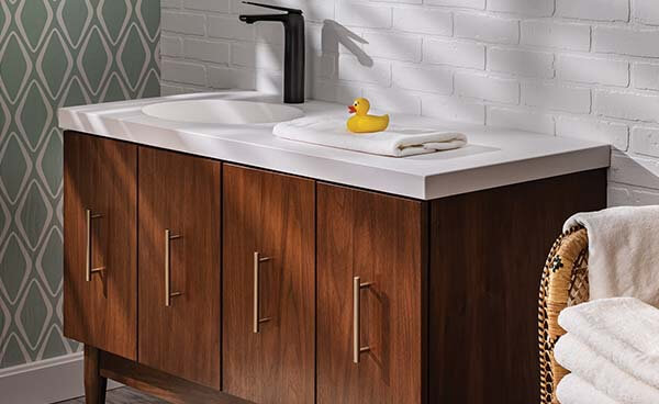 Modern bathroom vanity with black faucet, white counter, and medium wood base with gold vertical handles